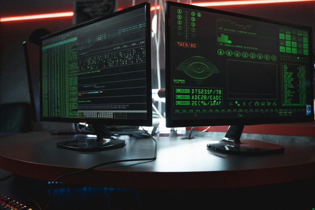 Dual computer monitors displaying code on a dark, red-lit desk