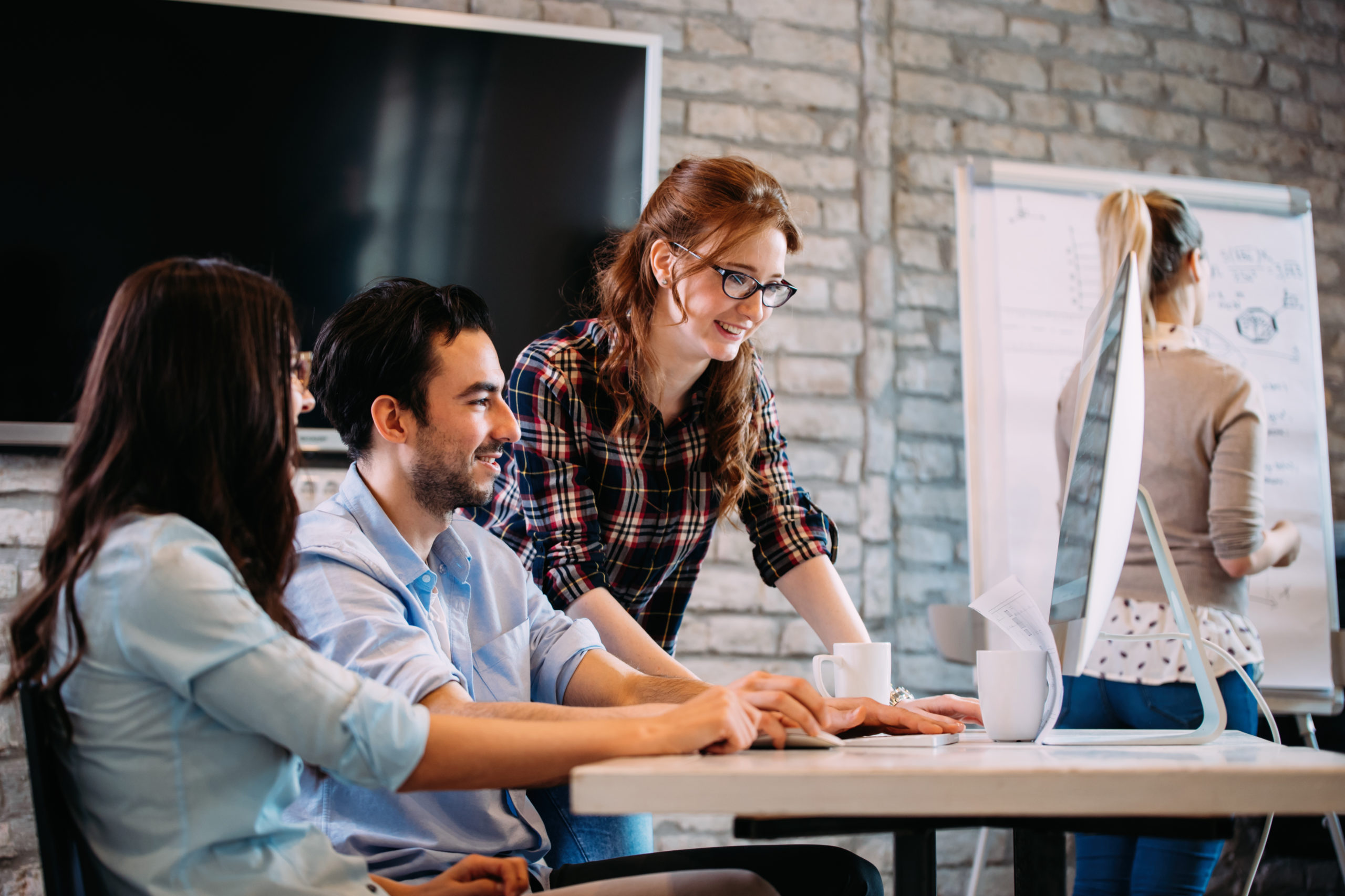 Team collaborating around a computer with a whiteboard in the background