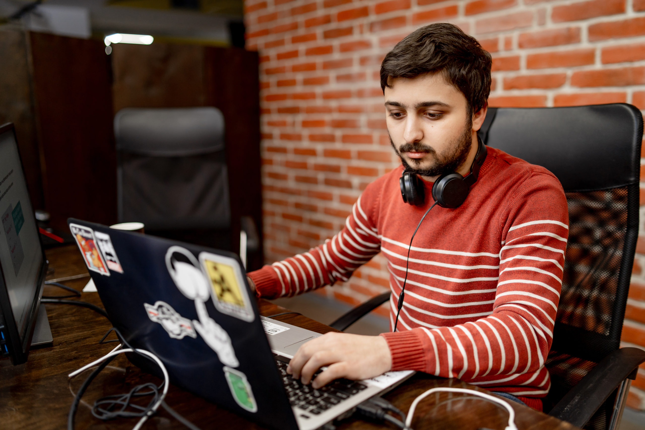 Developer working on a sticker-covered laptop against a brick wall