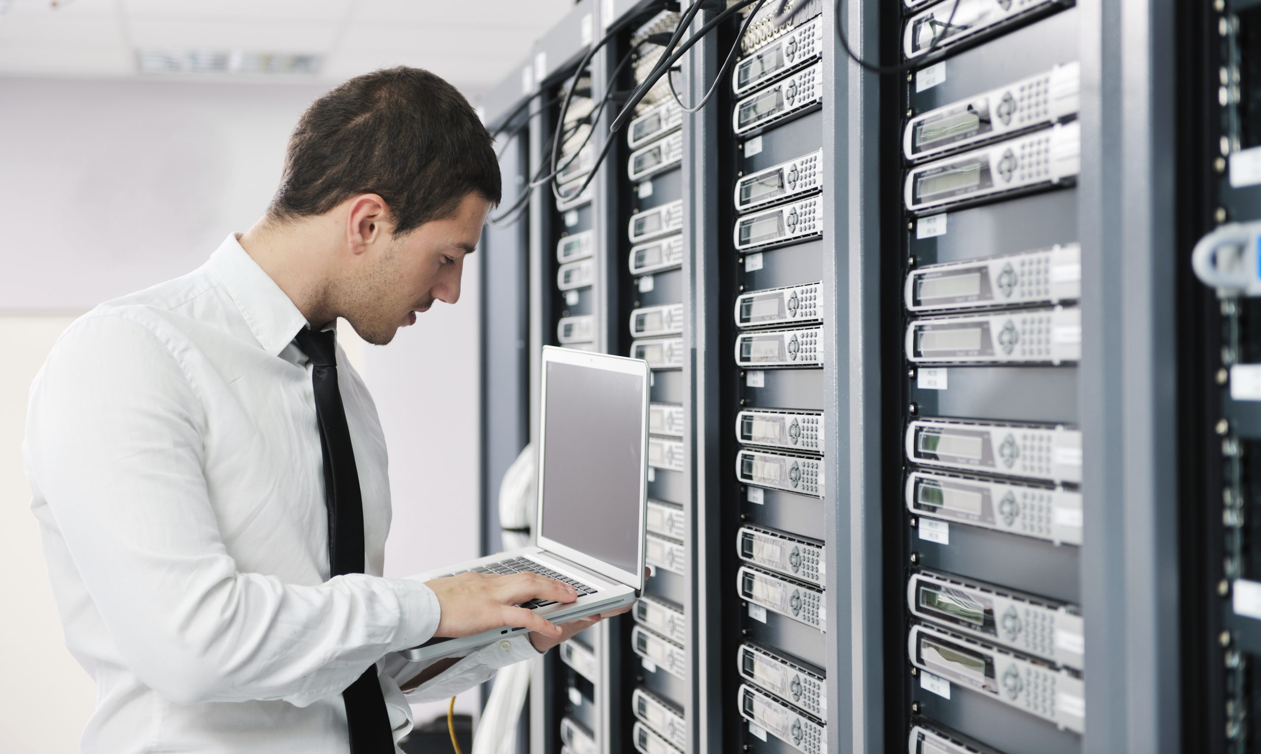 IT professional checking server racks while holding a laptop